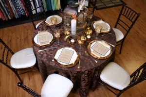Items shown: Raspberry truffle linen, Gold nova napkin, Mahogany chiavari chair with champagne cushion,  Gold mache glass charger plate, Ivory dinner plate, Aztec gold flatware, Gold glass votive cup Amber goblet.