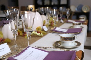Items shown: Farm Table, Natural Hemstitch overlay, Prairie Runner, Oak cross back chairs with natural cushion, Glass gold bead charger, Baroque cup and saucer, Gold rim glassware, Priscilla flatware.